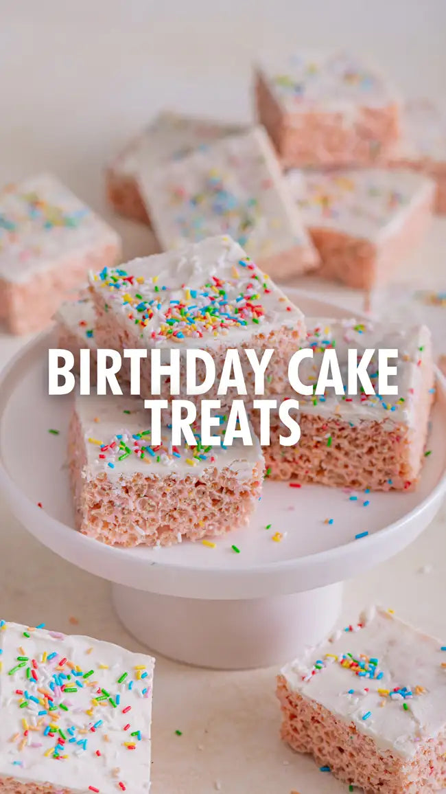 Birthday cake rice krispies treats with white icing and colorful sprinkles on a white pedestal plate.