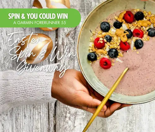 A golden-handled spoon rests in a light green bowl filled with pink smoothie topped with blueberries, raspberries, and granola.