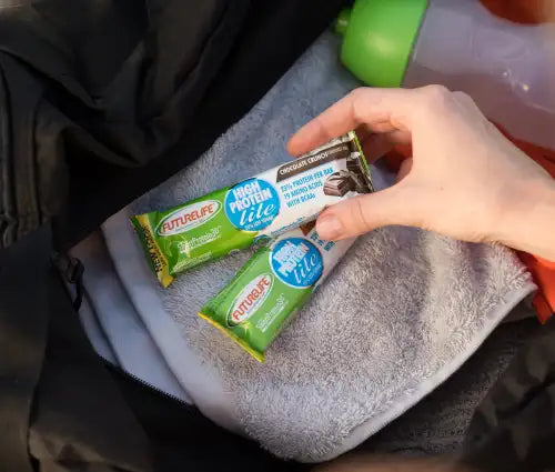 A hand holds a green and white futurelife high protein bar, with chocolate flavor packaging featuring nutritional information.