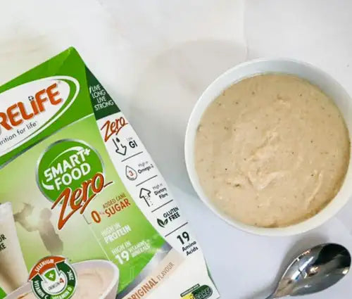 White bowl with creamy beige soup and spoon beside it, featuring a green box of smart+food zero protein powder.