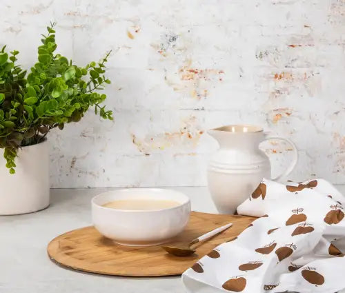 White ceramic pitcher with gold accents and apple print cloth.